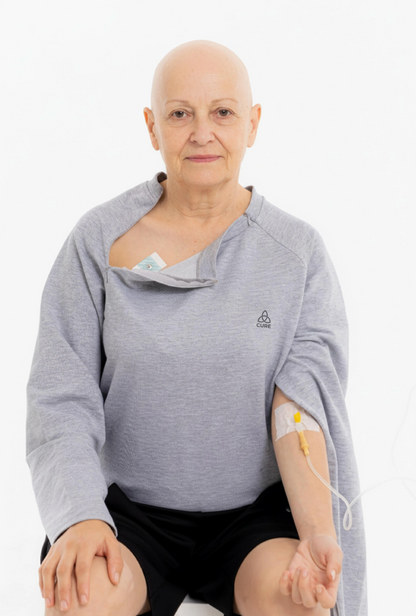 ComfortCure adaptif kemoterapi tedavi kıyafeti giymiş kadın hasta, kol fermuarı açık şekilde damar yolu erişimi sağlanıyor